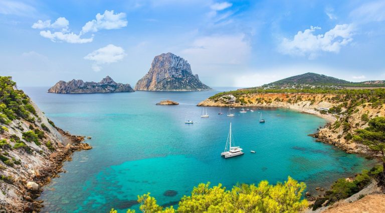 Vista de un mar turquesa con barcos y una isla rocosa al fondo.